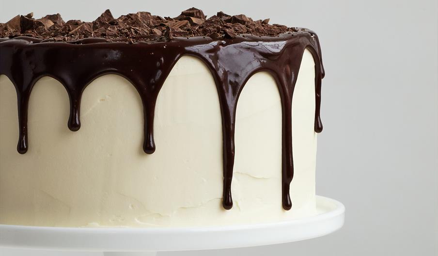 White cake on stand with melted dark chocolate topping